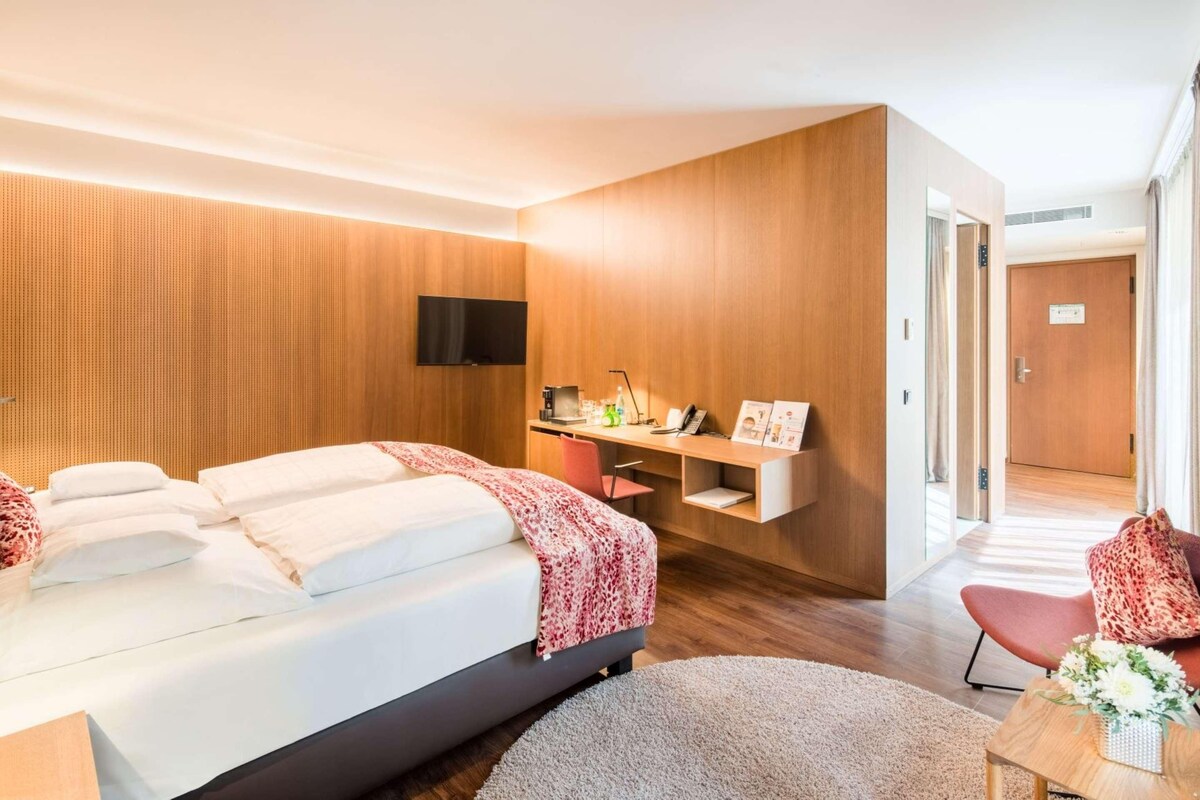 A modern hotel room with a large bed, a desk, a flat-screen TV, and a small seating area.