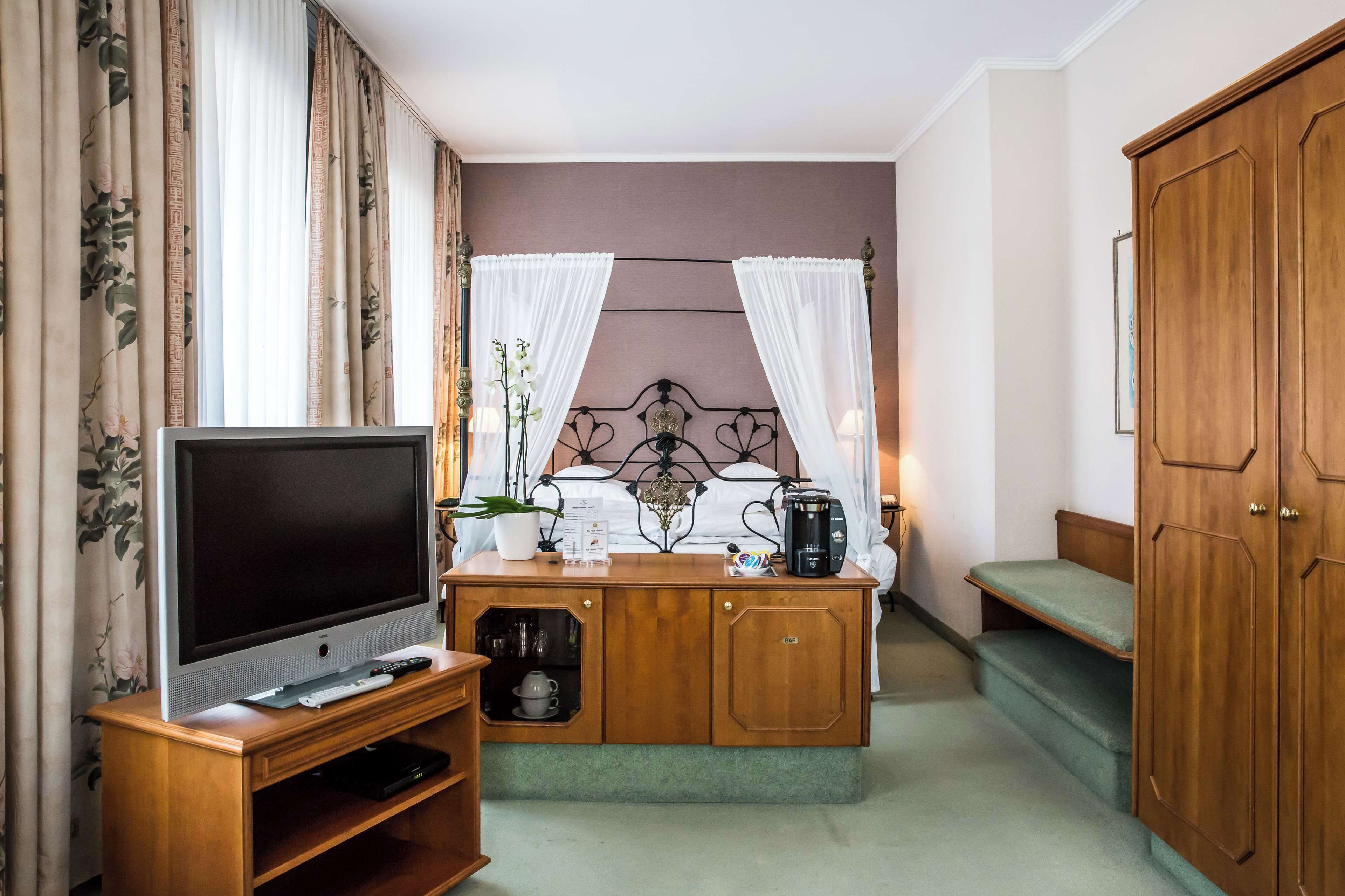 A compact hotel room with a television, a small cabinet with a coffee maker, a bed with a headboard, and a wardrobe.