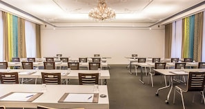 A conference room with rows of tables and chairs, a chandelier, and patterned curtains.
