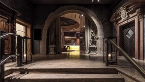 A grand staircase leading to a lobby with stone walls, a chandelier, and a statue.
