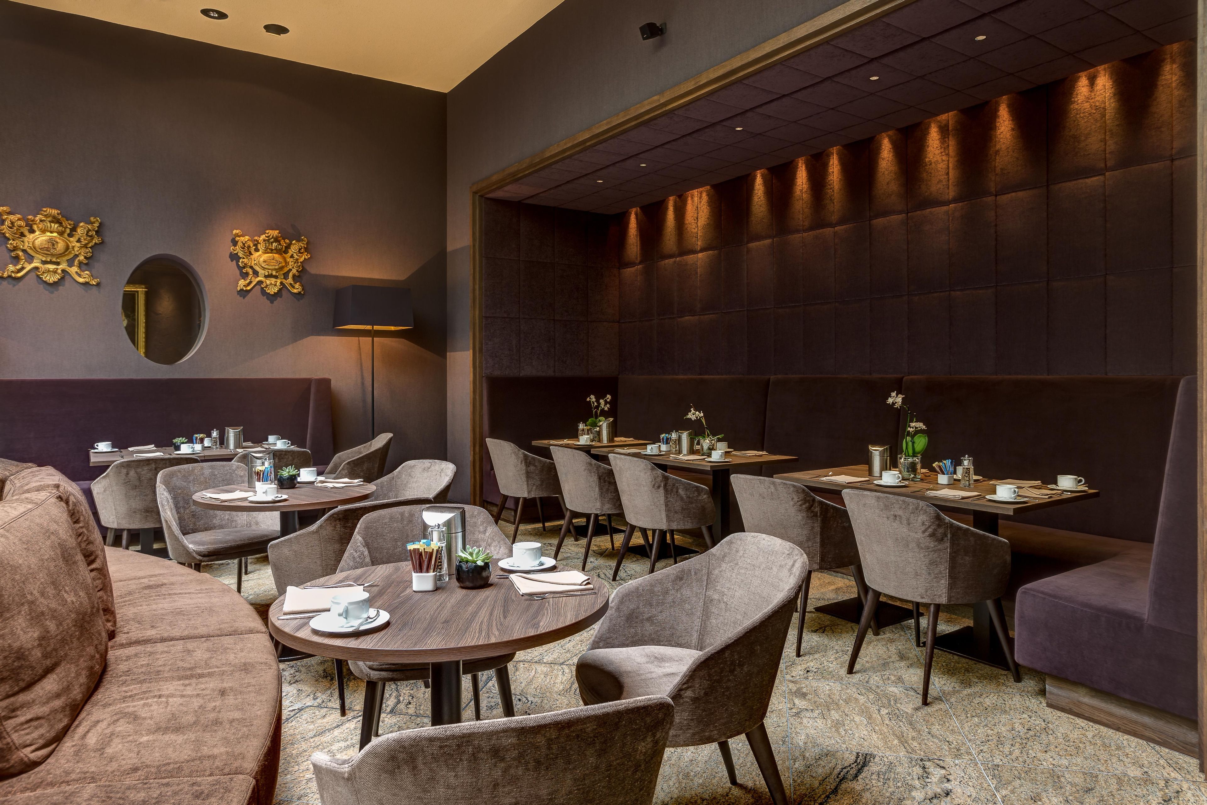 A modern dining area with round tables, cushioned chairs, and a dark, textured wall.