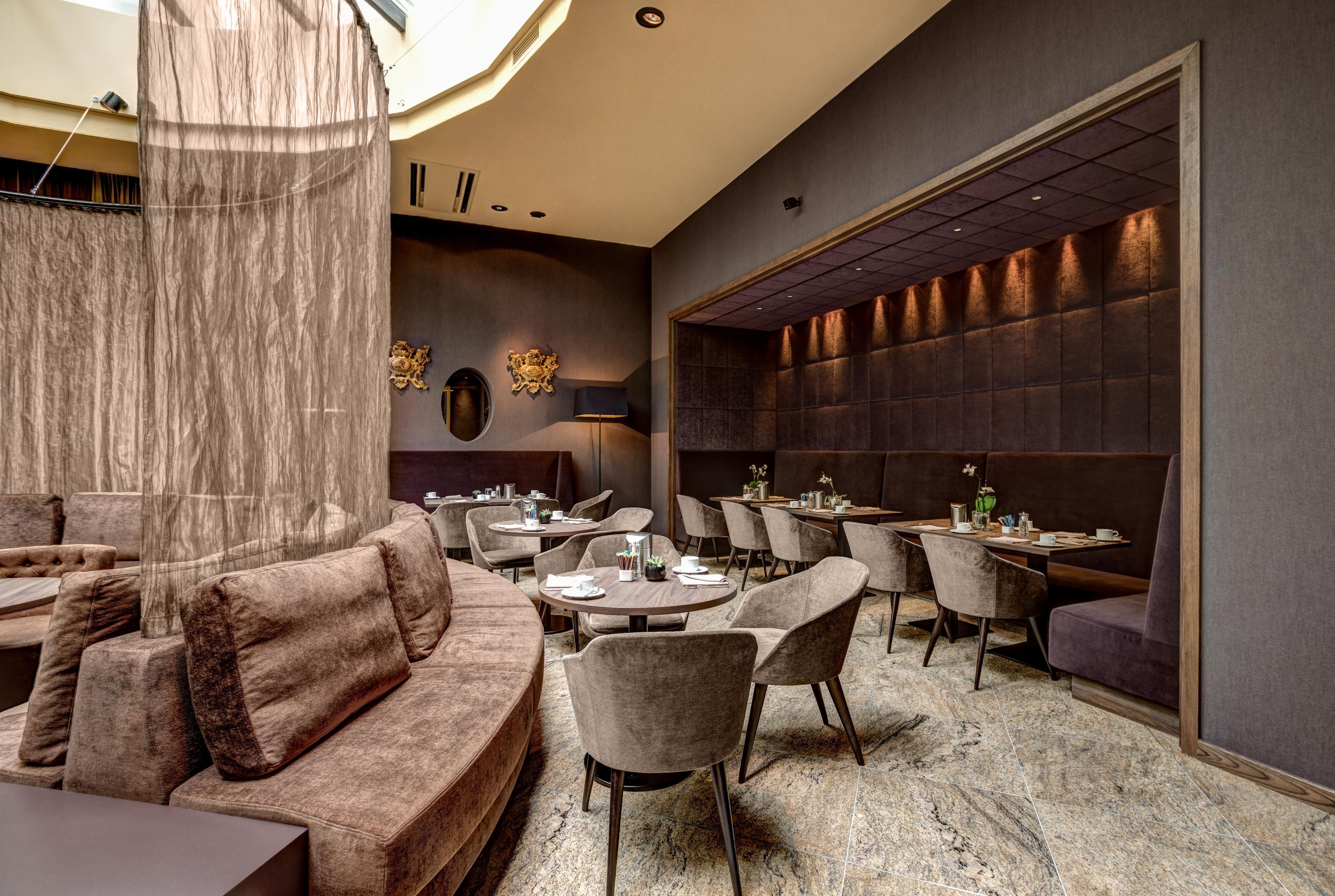 A modern restaurant interior with plush seating, round tables, and a decorative wall.