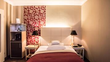 Ein Hotelzimmer mit Bett, Nachttischen, einer Lampe, einem Telefon, einer Kaffeemaschine und einem Ablagefach mit Pflegeartikeln.
