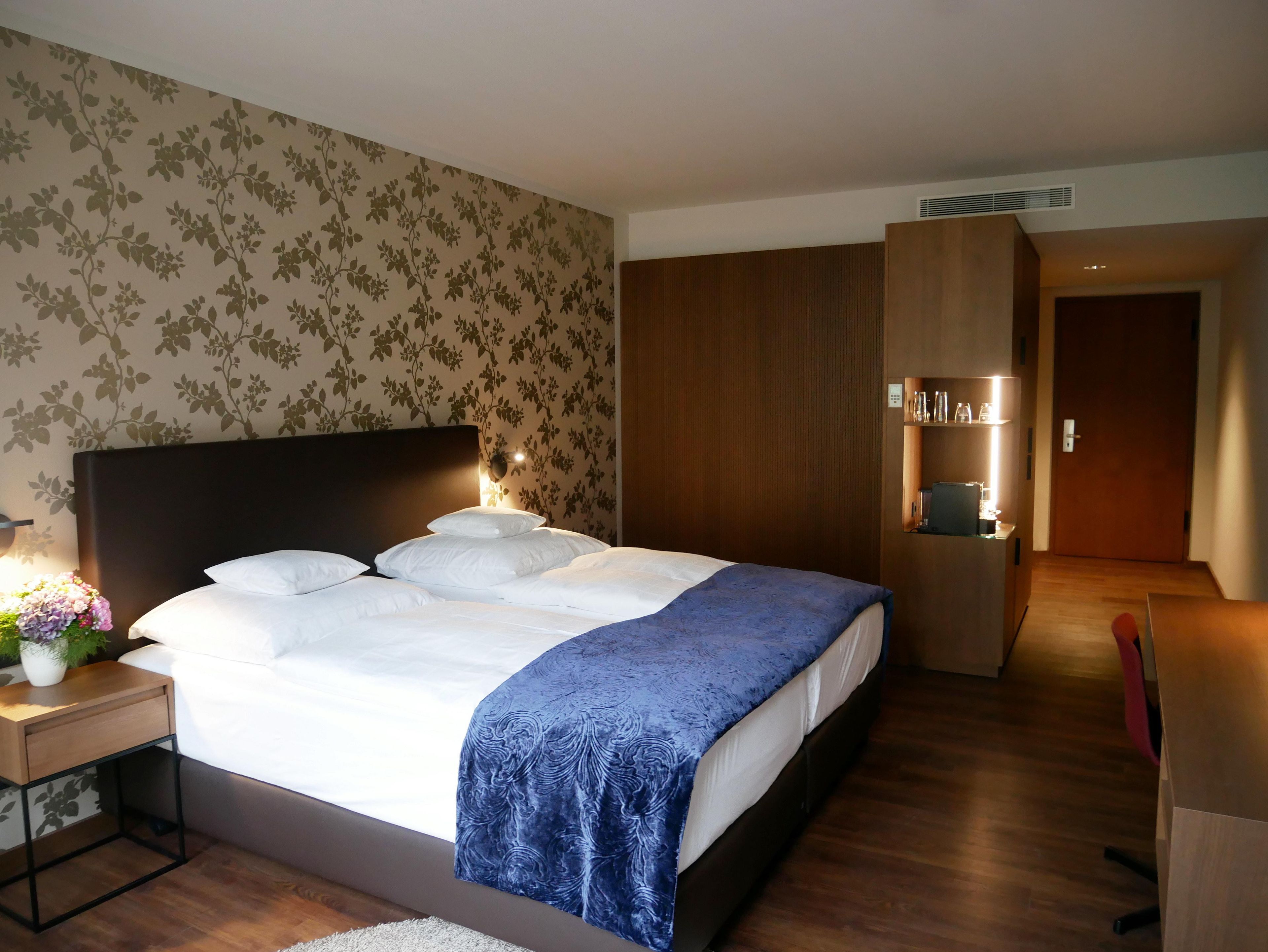 A hotel room with a bed, bedside table, lamp, and a wooden wardrobe.