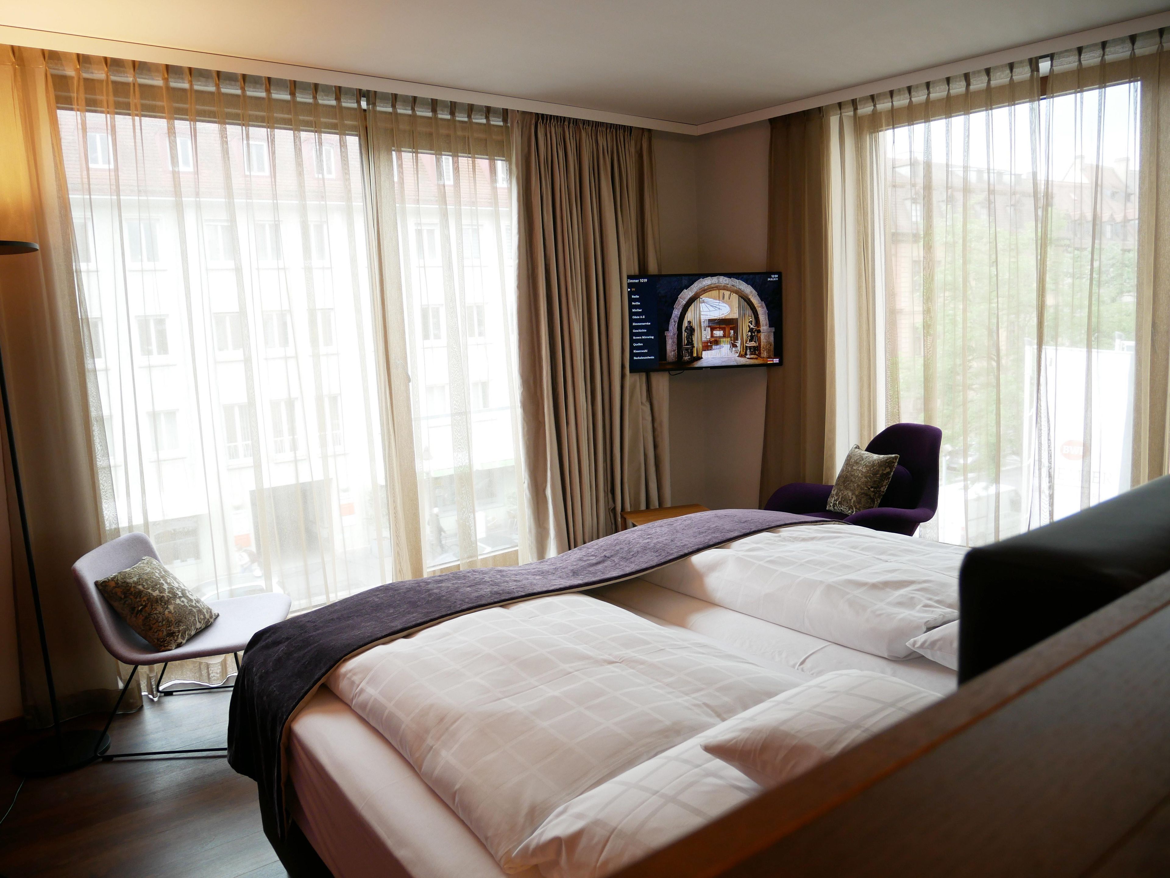 A hotel room with a large bed, a television mounted on the wall, and a chair.