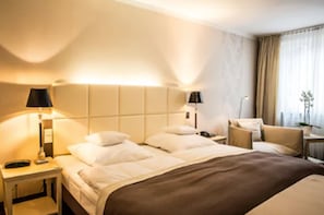 A hotel room with a bed, bedside tables, lamps, a chair, and a window with curtains.