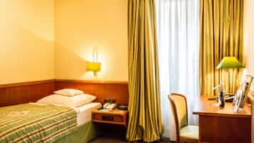 A hotel room with a bed, a nightstand, a desk with a lamp, and a chair.