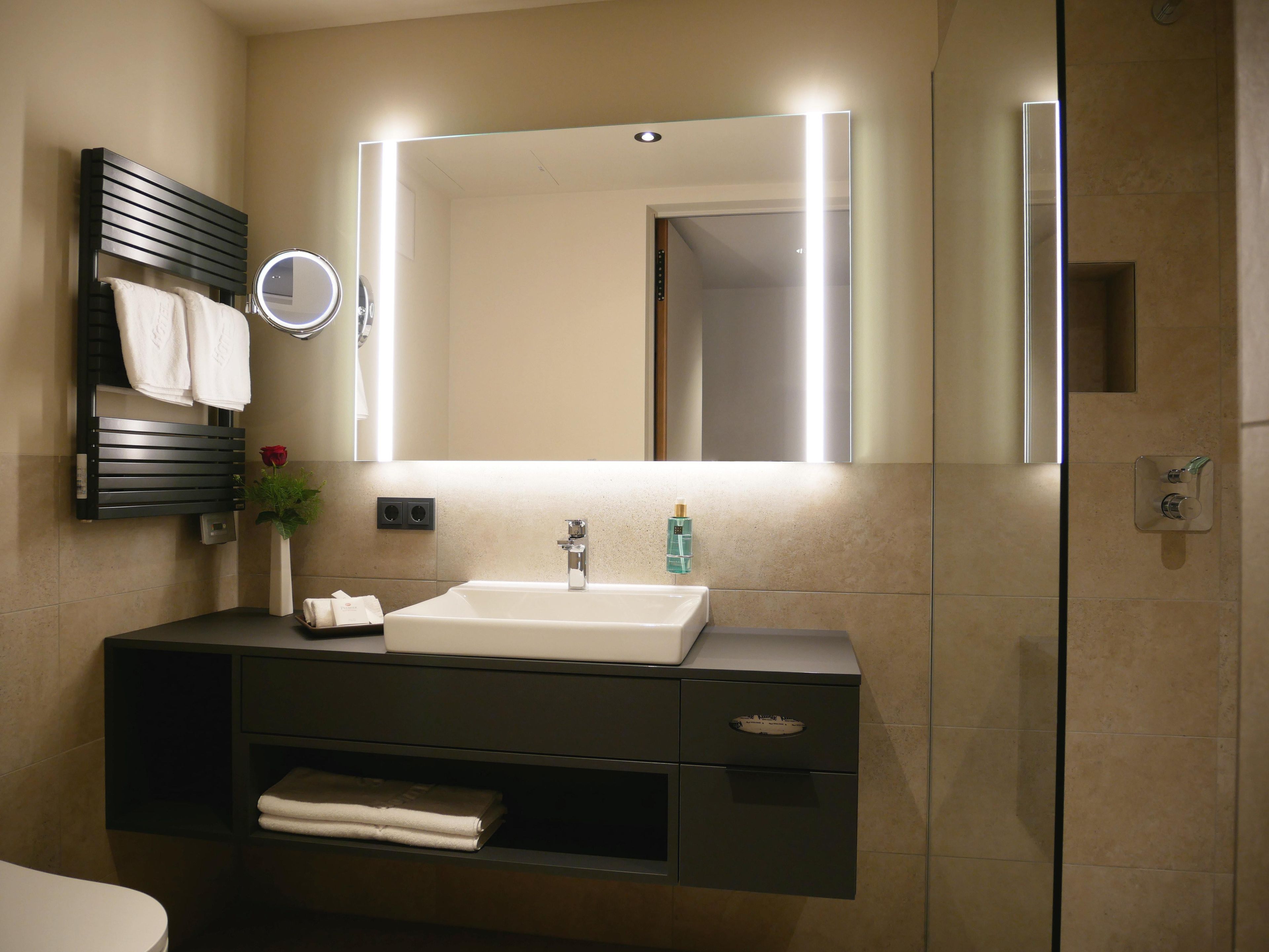A modern bathroom with a vanity, mirror, and a shower area.
