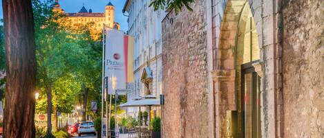A street view with a historic building, a clear sky, and a distant castle.