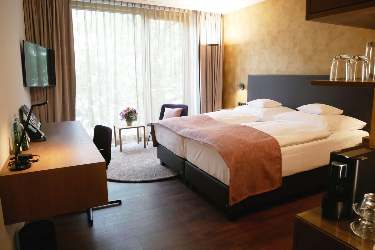 A hotel room with a bed, desk, chair, and a TV mounted on the wall.
