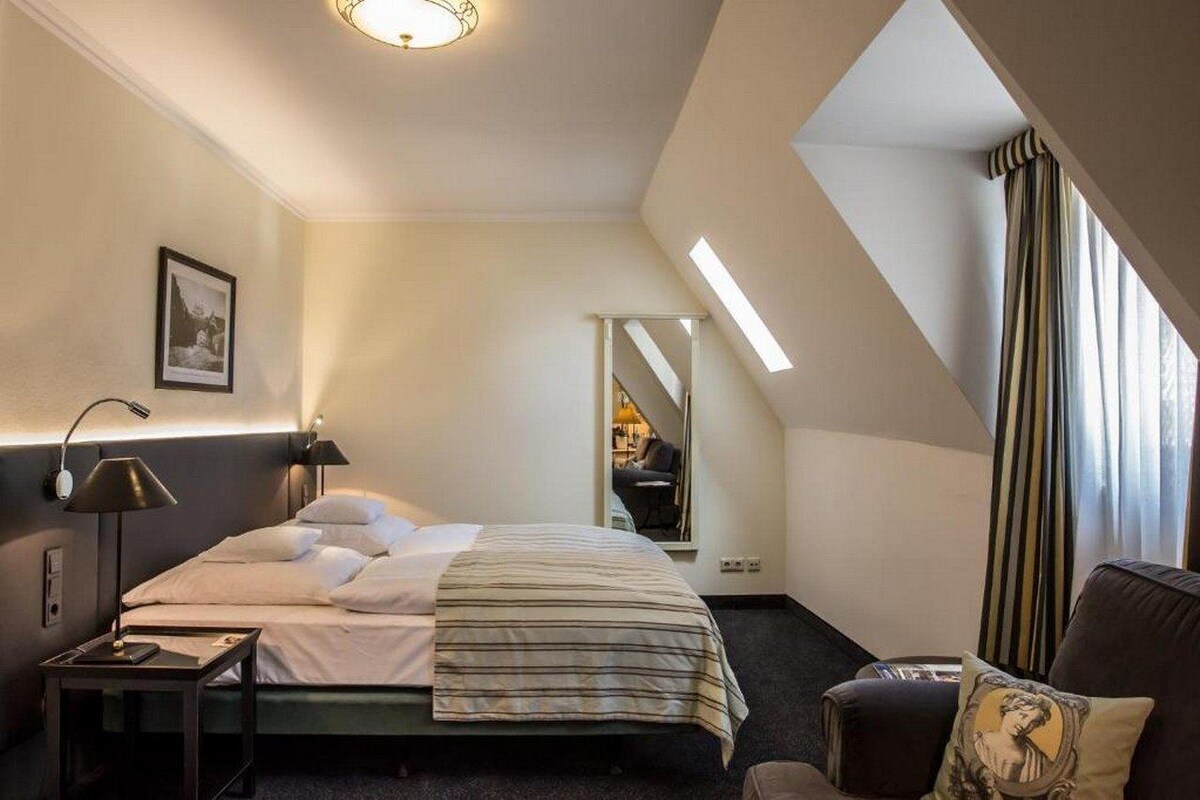 A hotel room with a bed, bedside table, lamp, and a mirror.