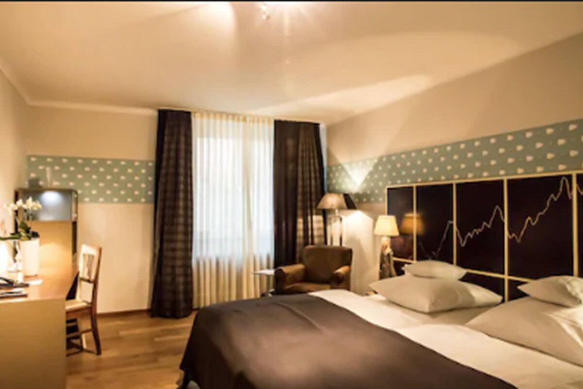A hotel room with a bed, a desk, a chair, and a window with curtains.