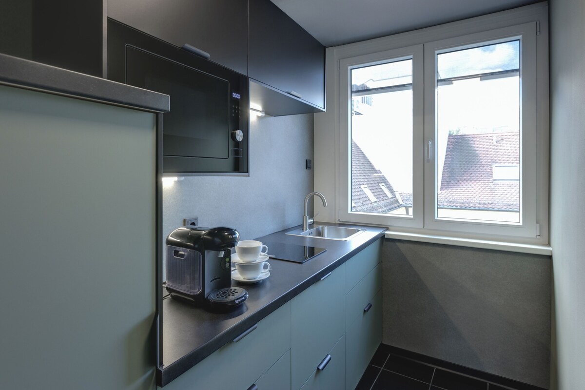 A modern kitchen with a built-in coffee maker, a sink, and a window overlooking a residential area.