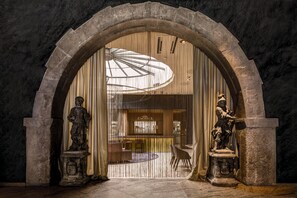 An arched doorway with two statues on pedestals, a circular table, and a patterned curtain. - Best Western Premier Hotel Rebstock (Würzburg)