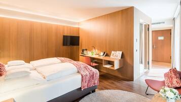 Quarto de hotel moderno com cama, escrivaninha, TV de tela plana e porta de acesso a outro cômodo.