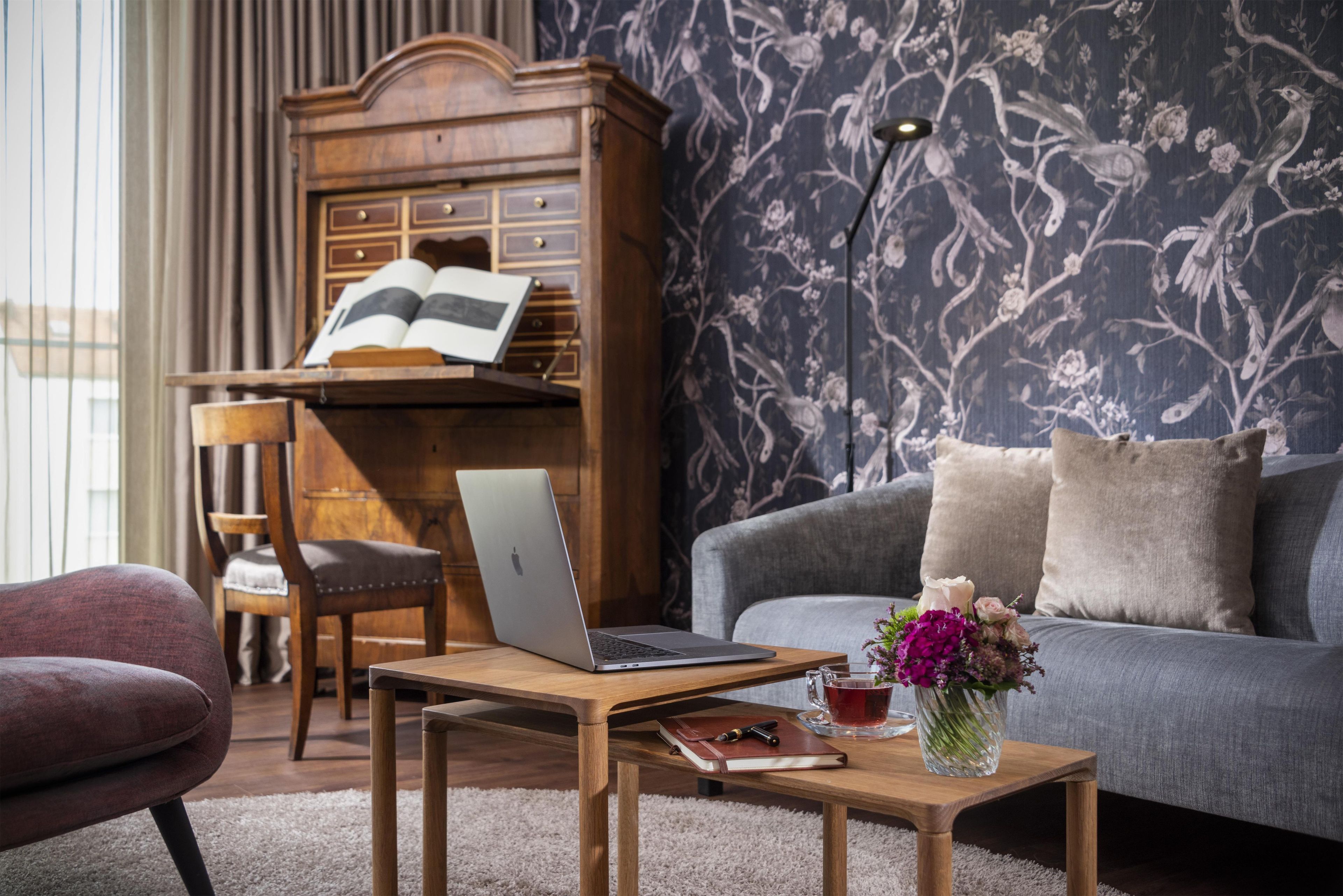 Ein modernes Wohnzimmer mit einer Couch, einem Holztisch, einem Laptop, einem Buch und einer Vase mit Blumen.