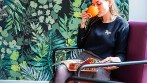 A person sitting on a purple chair with a magazine, in front of a wall with a leafy pattern. - ibis Styles Perpignan Centre Gare (Perpignan)