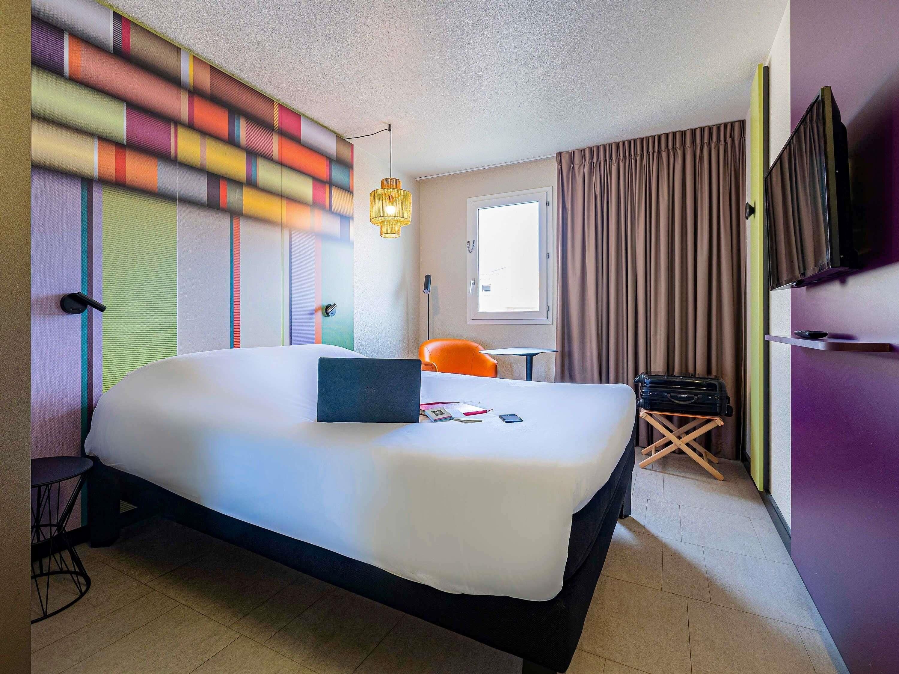 A hotel room with a large bed, a desk, a chair, a television, and a window with curtains.