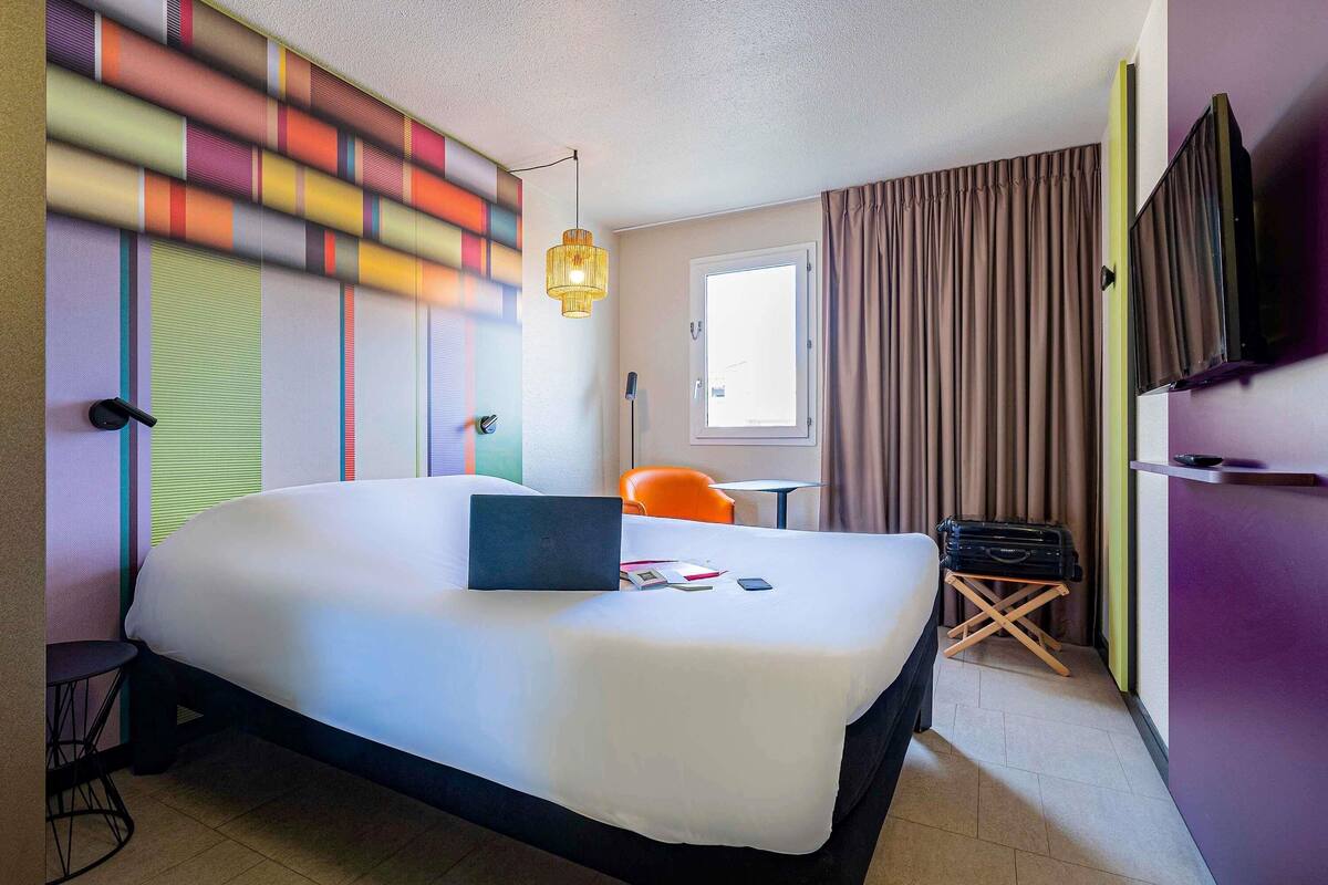 Une chambre d’hôtel avec un grand lit, un bureau, une chaise, une télévision et une fenêtre avec des rideaux.