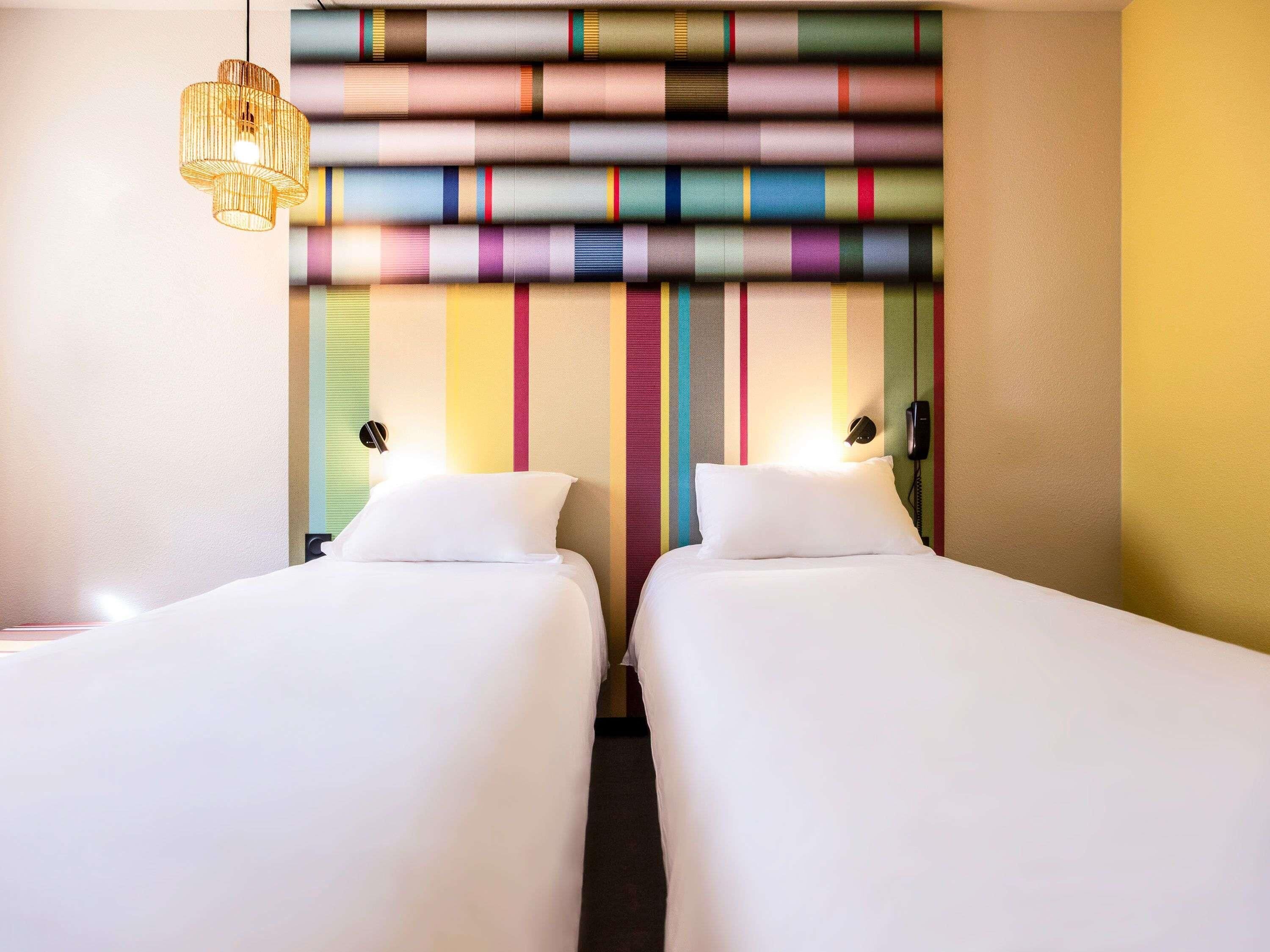 A hotel room with two beds, a striped wall, a hanging light fixture, and a phone on the wall.