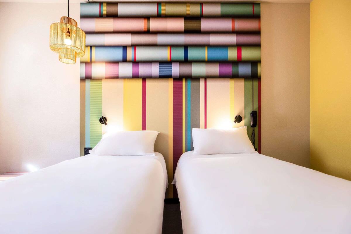 Une chambre d’hôtel avec deux lits, un mur à rayures, un luminaire suspendu et un téléphone fixé au mur.