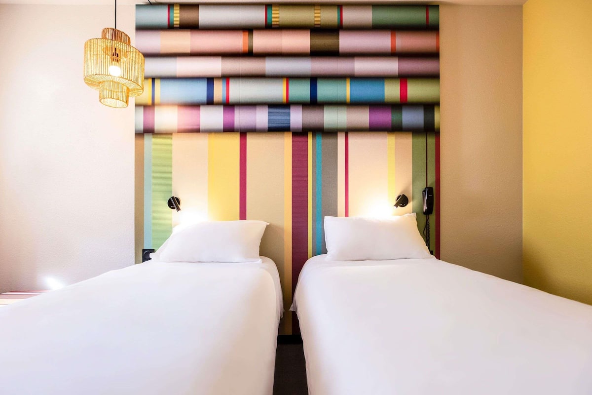 A hotel room with two beds, a striped wall, a hanging light fixture, and a phone on the wall.