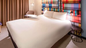 A hotel room with a large bed, a chair, a small table, and a colorful wall. - ibis Styles Perpignan Centre Gare (Perpignan)
