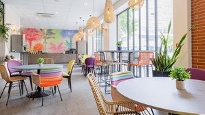 A modern dining area with round tables, colorful chairs, wicker seating, and large windows with a city view. - ibis Styles Perpignan Centre Gare (Perpignan)