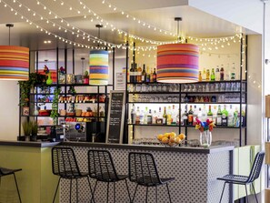 A bar area with striped lamps, shelves of bottles, and black chairs. - ibis Styles Perpignan Centre Gare (Perpignan)