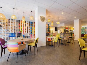 Relax in a stylish space with round tables, colorful chairs, and a vibrant patterned wall.