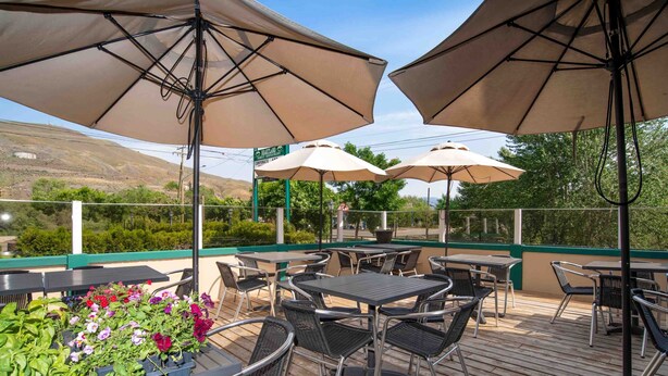 An outdoor patio with tables and chairs, shaded by large umbrellas, and surrounded by greenery and hills. - Sandman Inn Cache Creek (Cache Creek)