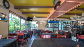 A restaurant with wooden tables and chairs, a bar area with shelves of bottles, and a view of greenery outside. - Sandman Inn Cache Creek (Cache Creek)