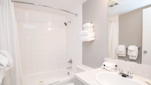 A modern bathroom with a bathtub, toilet, and sink. There are towels stacked on the wall and a mirror above the sink.