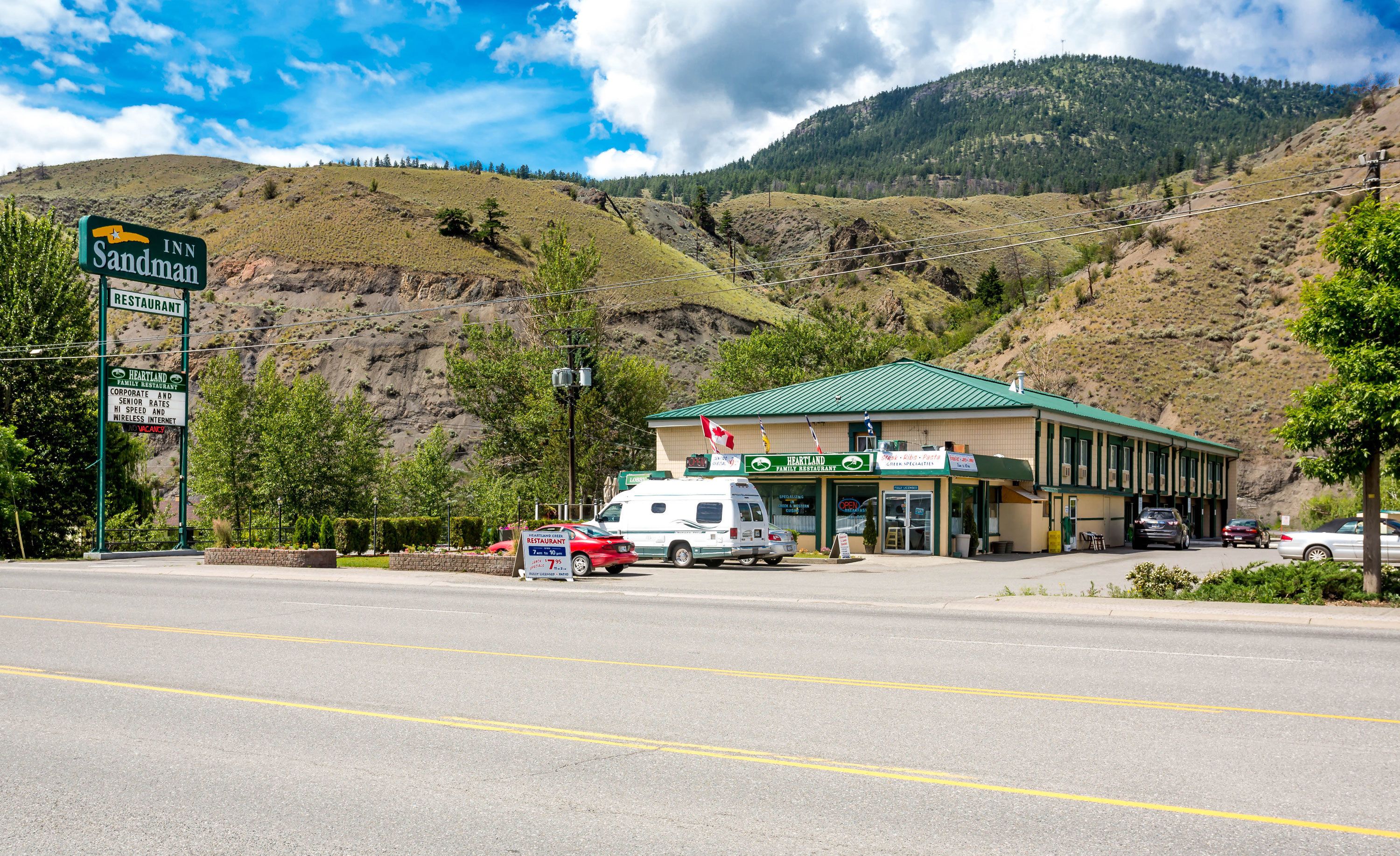 A Heartland Family Restaurant with a green roof, located at a roadside with a mountainous backdrop.