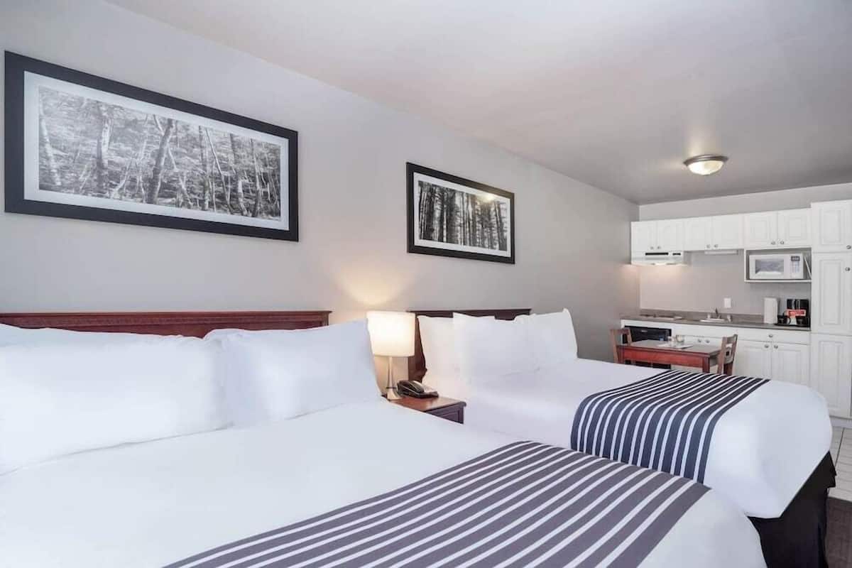 A hotel room with two beds, a kitchenette, and framed pictures on the wall.