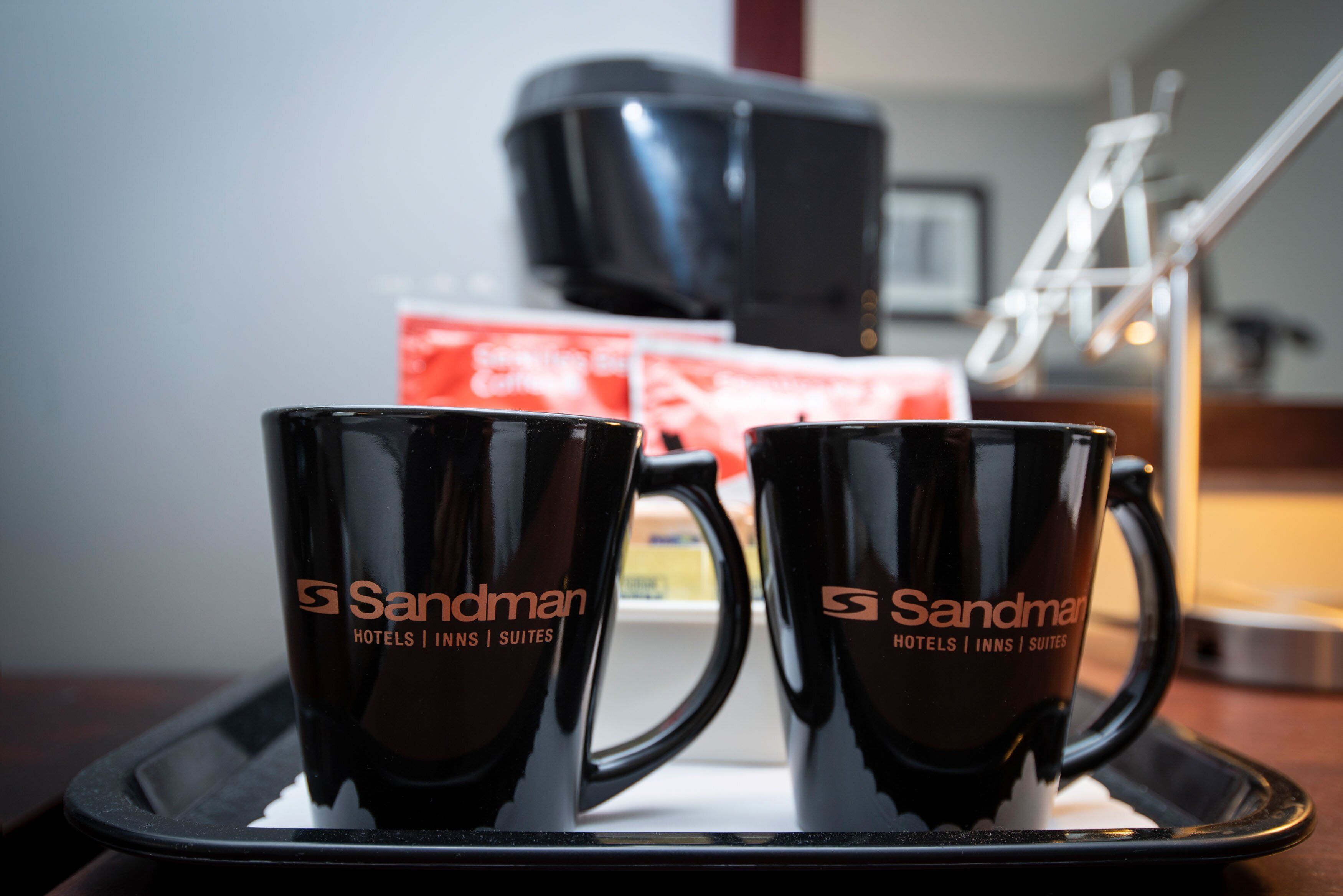 Two black mugs with the Sandman Hotels logo on a tray.