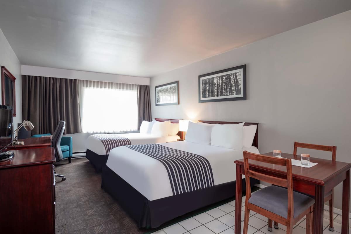 A hotel room with two beds, a desk, a chair, a table, and a TV.