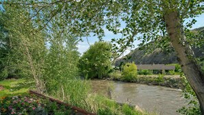 A river with a wooden bridge, surrounded by lush greenery and a building in the background. - Sandman Inn Cache Creek (Cache Creek)
