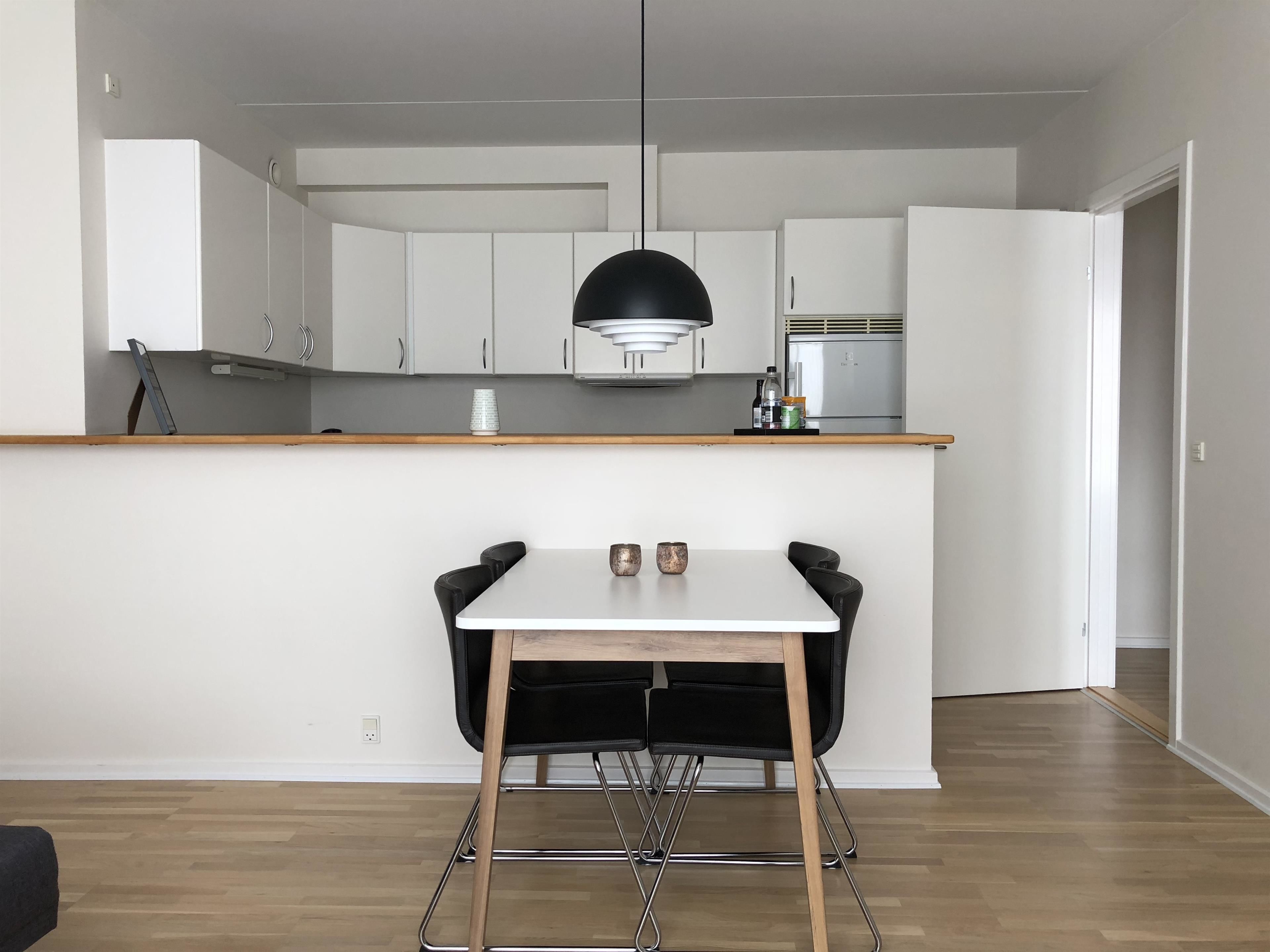 Et moderne køkken med hvide skabe, en træbordplade og en sort hængende lampe.