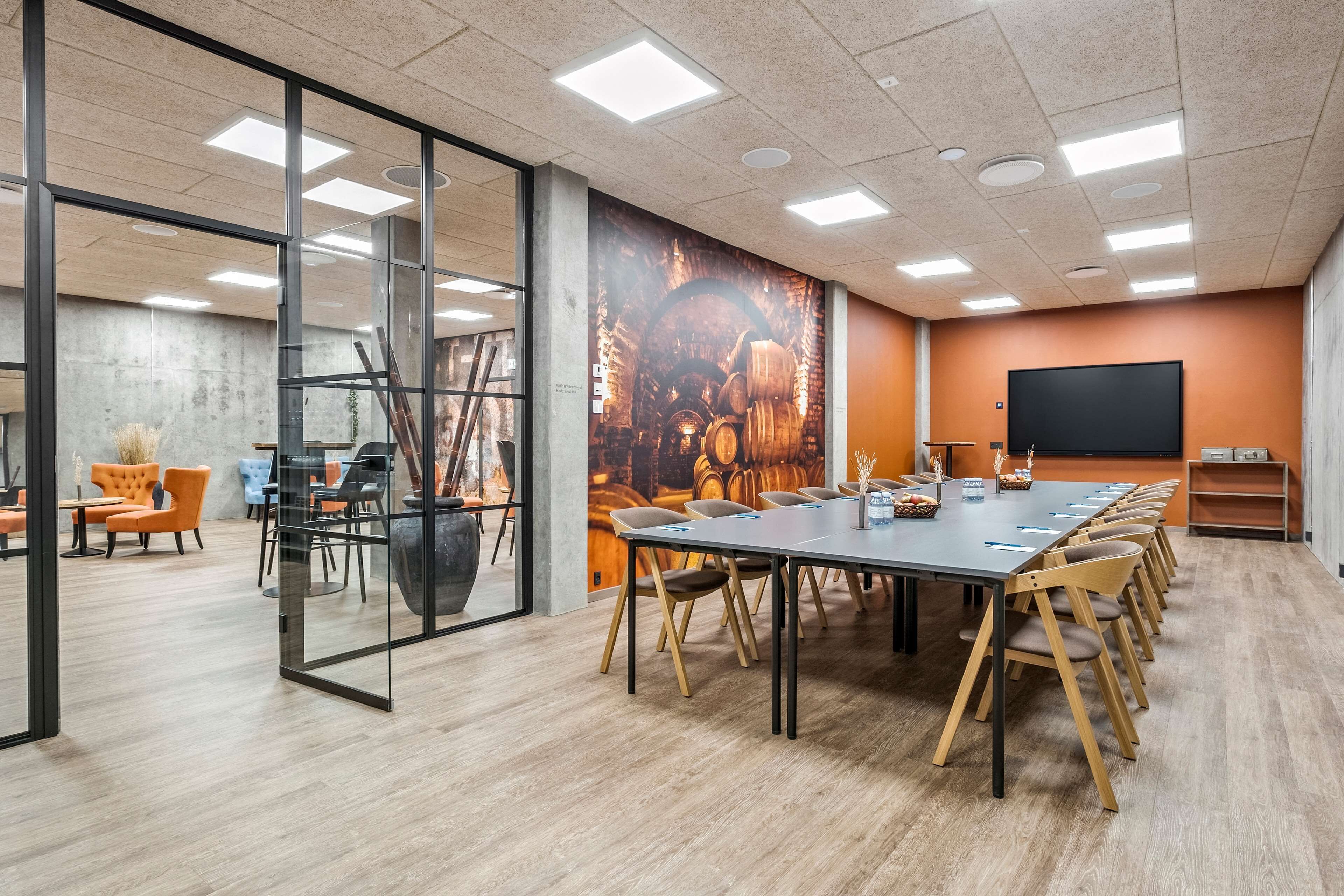 A conference room with a long table, chairs, a projector screen, and a mural on the wall.