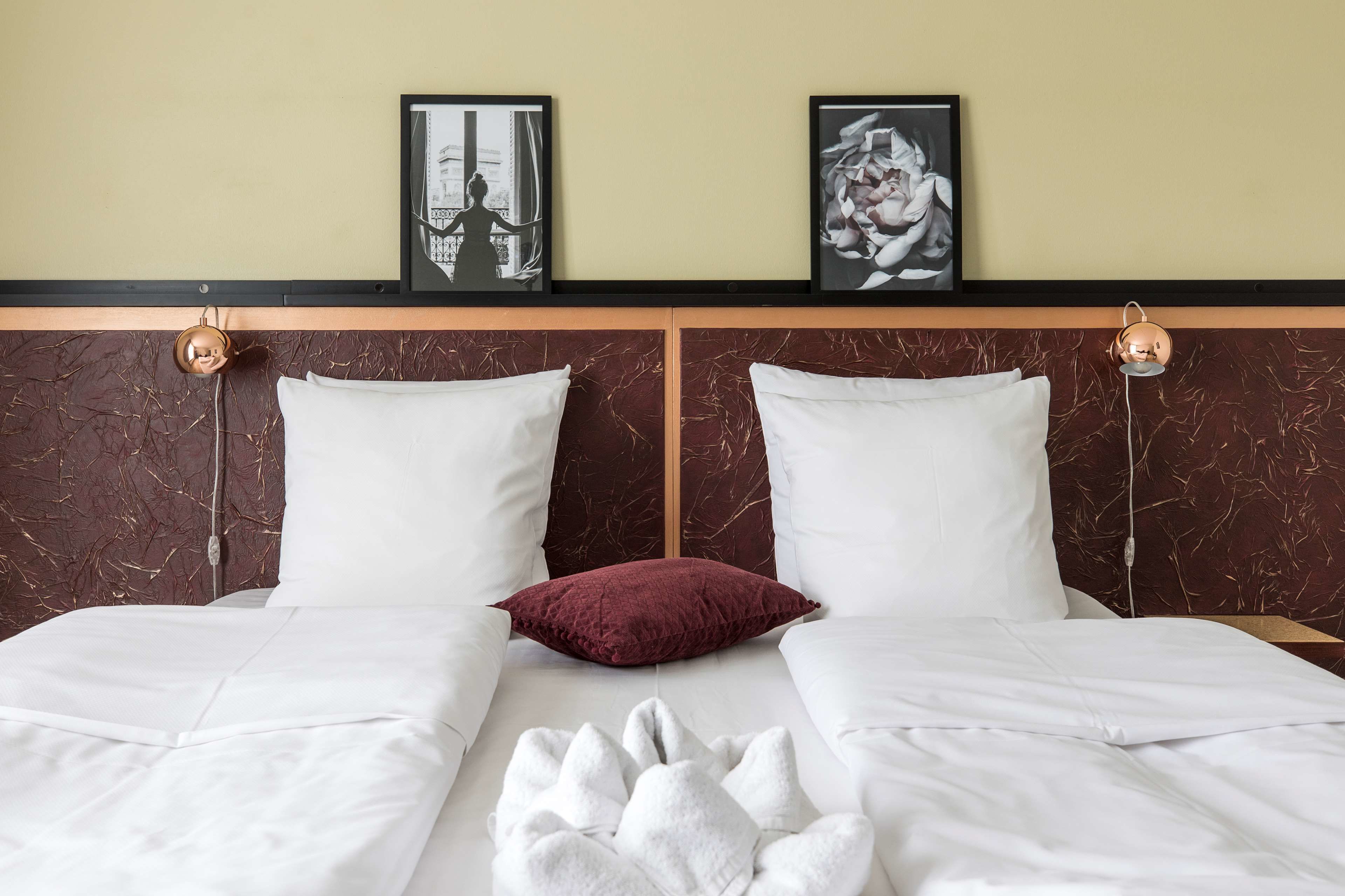 A hotel room with two beds, white bedding, a red pillow, and two framed pictures on the wall.