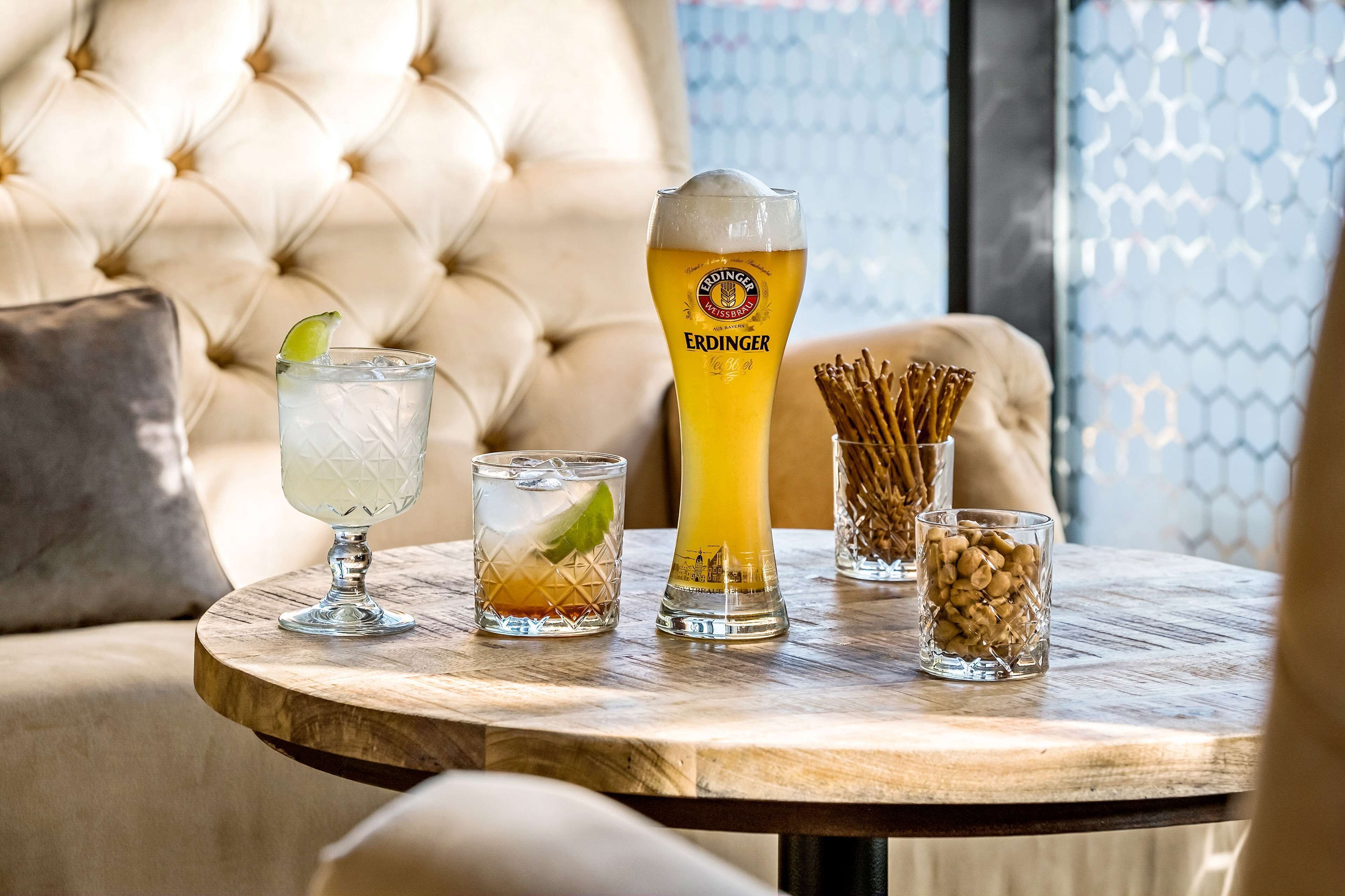 Una mesa redonda de madera con tres vasos de cerveza, uno con un gajo de lima y un vaso alto con la etiqueta "ERDINGER".