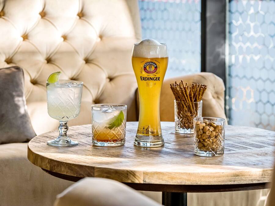 Una mesa redonda de madera con tres vasos de cerveza, uno con un gajo de lima y un vaso alto con la etiqueta "ERDINGER".
