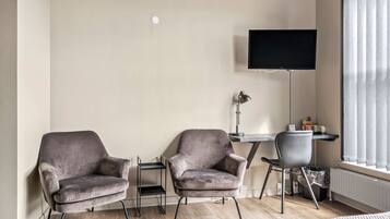 Una sala de estar moderna con dos sillones grises, una mesita, un televisor montado en la pared y un ventanal con cortinas.
