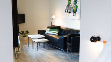 A modern living room with a black leather sofa, a white coffee table, and a floor lamp. There is a painting on the wall and a plant on the floor.