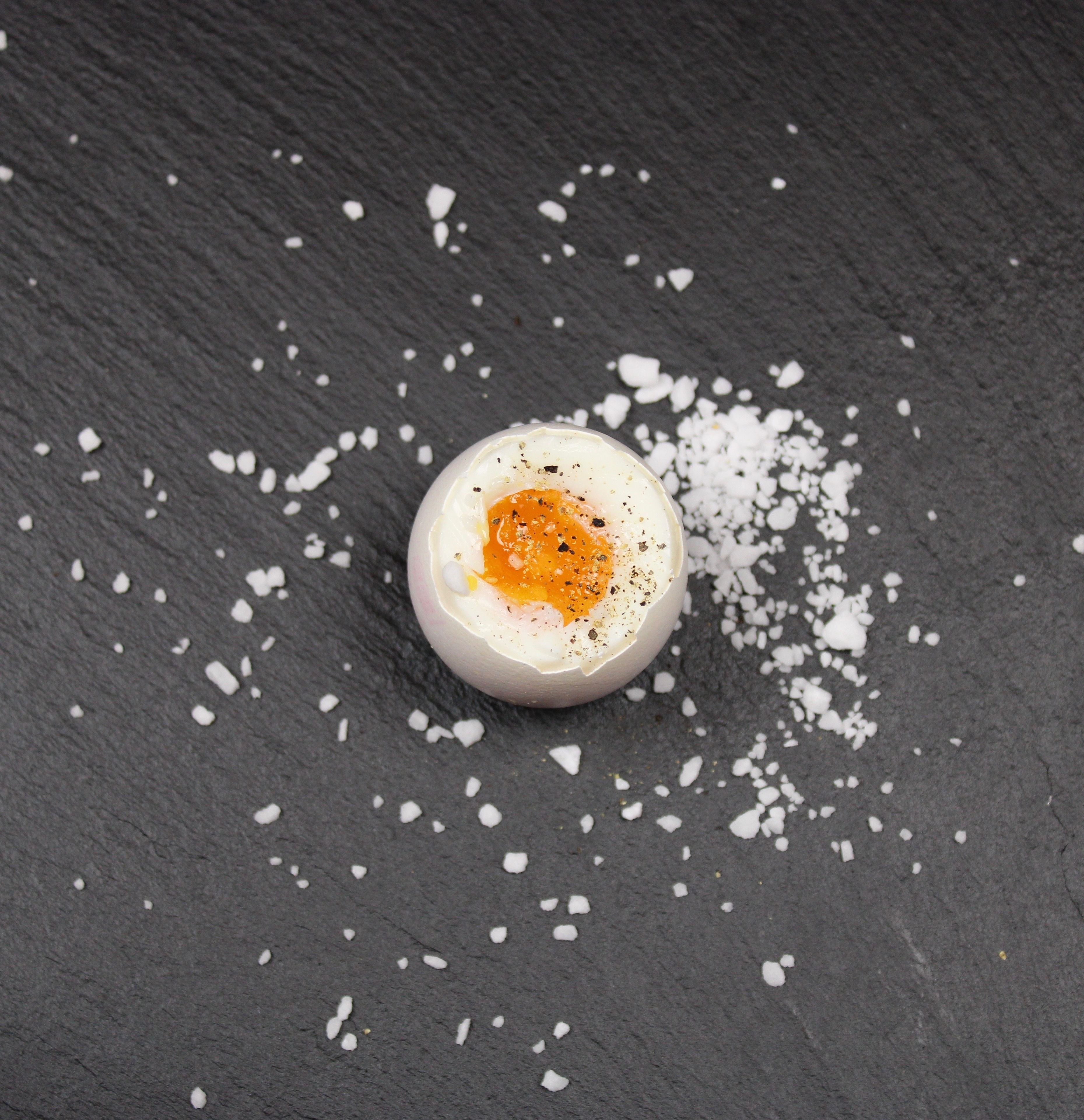 A single egg yolk on a dark surface with scattered salt crystals.