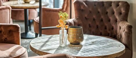 Una mesa de madera redonda con un jarrón de flores secas y una lámpara con textura.
