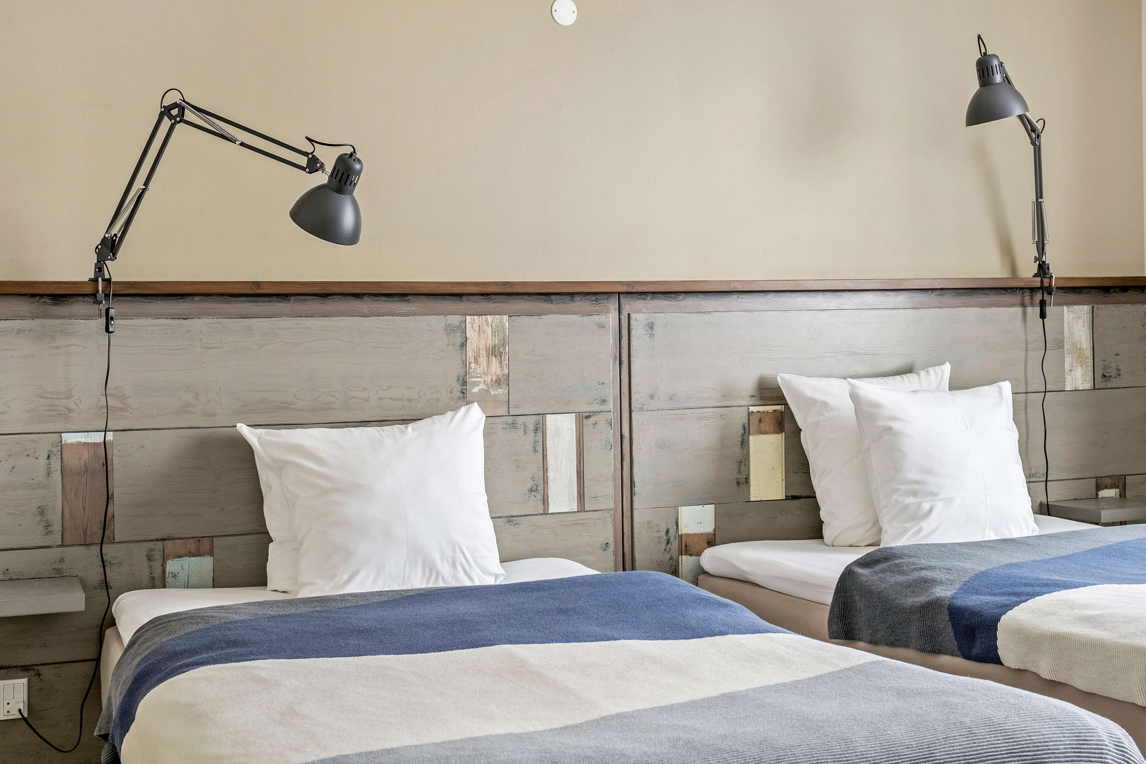 Habitación de hotel con dos camas, cada una con un almohadón blanco y una manta azul y blanca a rayas. Hay dos lámparas de escritorio negras a cada lado de las camas.