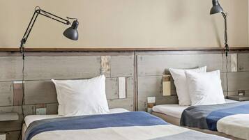 Habitación de hotel con dos camas, cada una con un almohadón blanco y una manta azul y blanca a rayas. Hay dos lámparas de escritorio negras a cada lado de las camas.