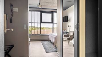 A modern hotel room with a large window, a bed, a desk, and a chair.